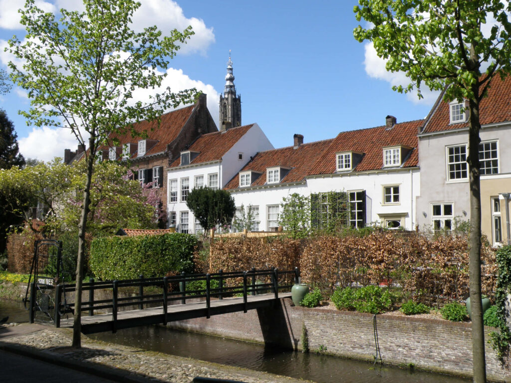 Amersfoort canal houses footbridge church tower lush greenery bright blue sky wallpaper background