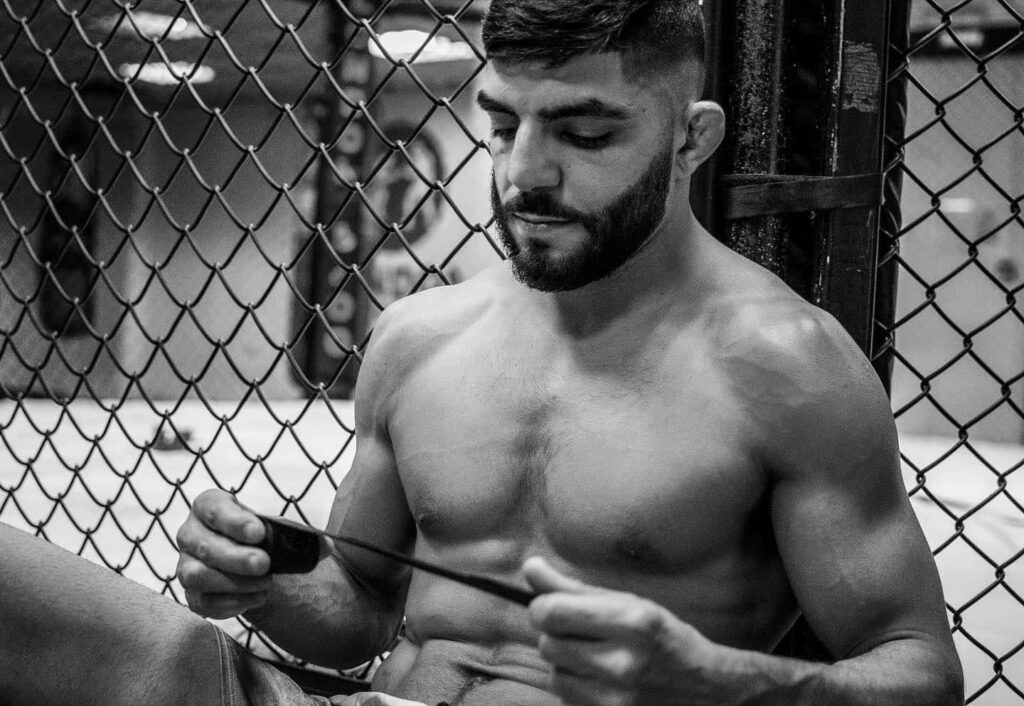 Amir Albazi focused wrapping hands against cage in gym preparing for MMA training session Wallpaper
