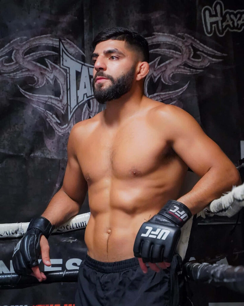 Amir Albazi relaxing on boxing ring ropes wearing UFC gloves black shorts gym background wallpaper