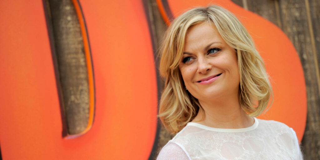Amy Poehler smiling proudly in front of vibrant colorful backdrop celebrating directorial debut Wallpaper