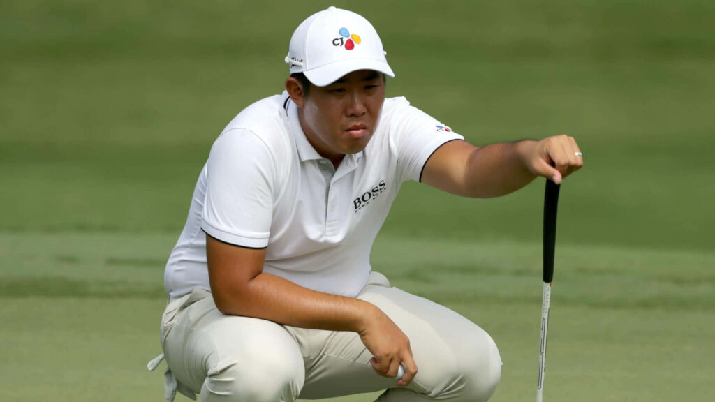 Golfer An Byeong-hun in white polo focused on golf course with lush green background wallpaper