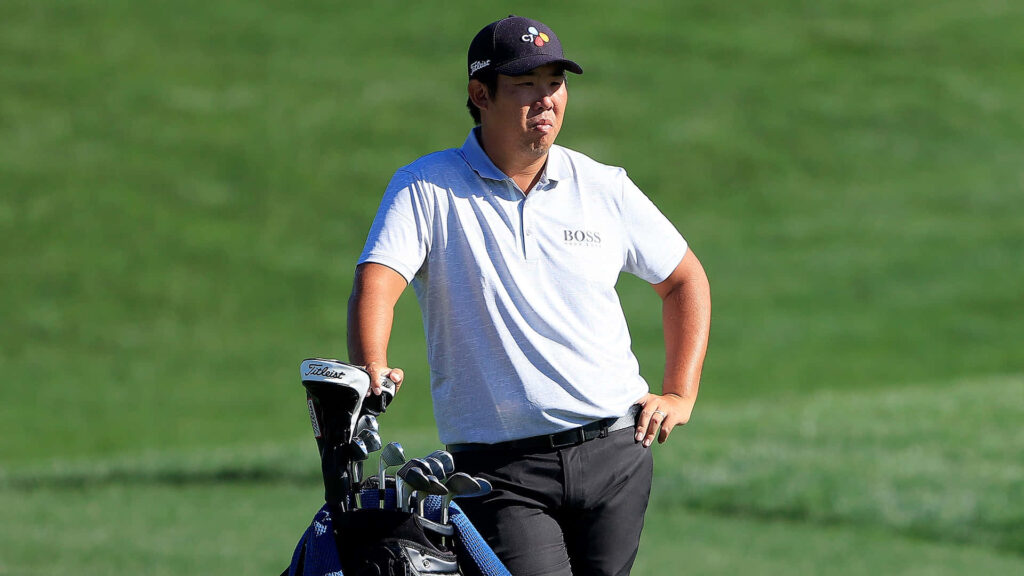 An Byeong-hun on lush green golf course wearing white polo and dark cap with golf bag nearby Wallpaper