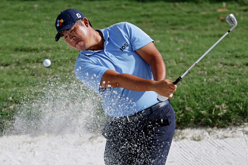 An Byeong-hun hitting a bunker shot with flying sand and focused energy on green golf course Wallpaper