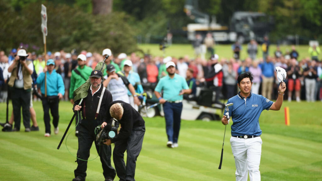 An Byeong-hun smiling and waving cap on vibrant green golf course during professional tournament Wallpaper
