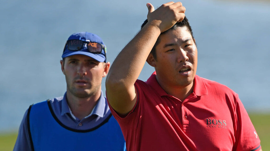 An Byeong-hun scratching head on sunny golf course wearing red BOSS polo with caddie blue shirt Wallpaper