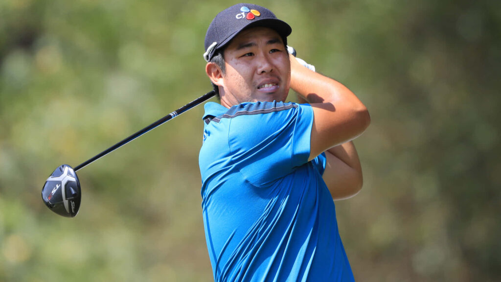 An Byeong-hun golf swing final pose focused expression blue shirt black cap outdoor background Wallpaper