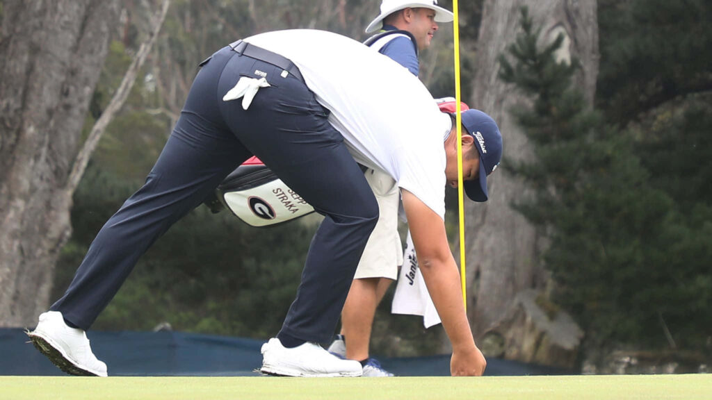 An Byeong-hun focused on golf course checking alignment stick in bright natural daylight wallpaper