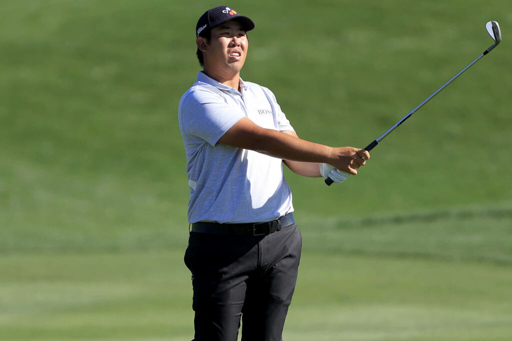 Byeong-hun An focused on golf course pointing club forward in gray polo and black pants outdoors Wallpaper