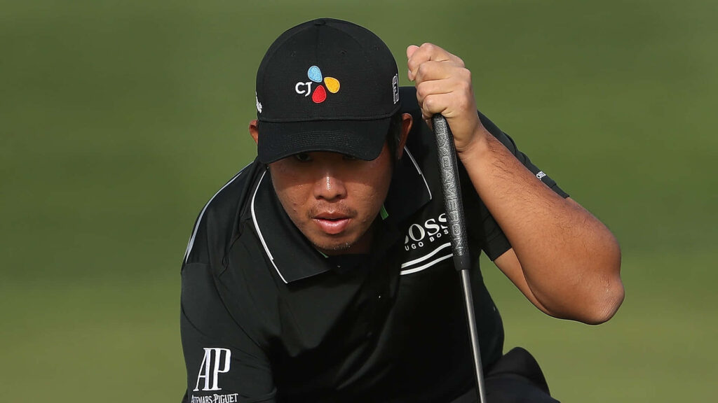 An Byeong-hun focused on golf green checking putting line in black attire and branded cap Wallpaper