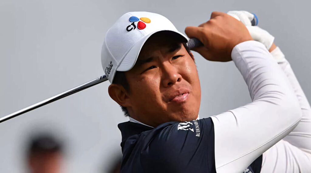 An Byeong-hun mid golf swing wearing white cap sporty arm protection on sunny golf course Wallpaper
