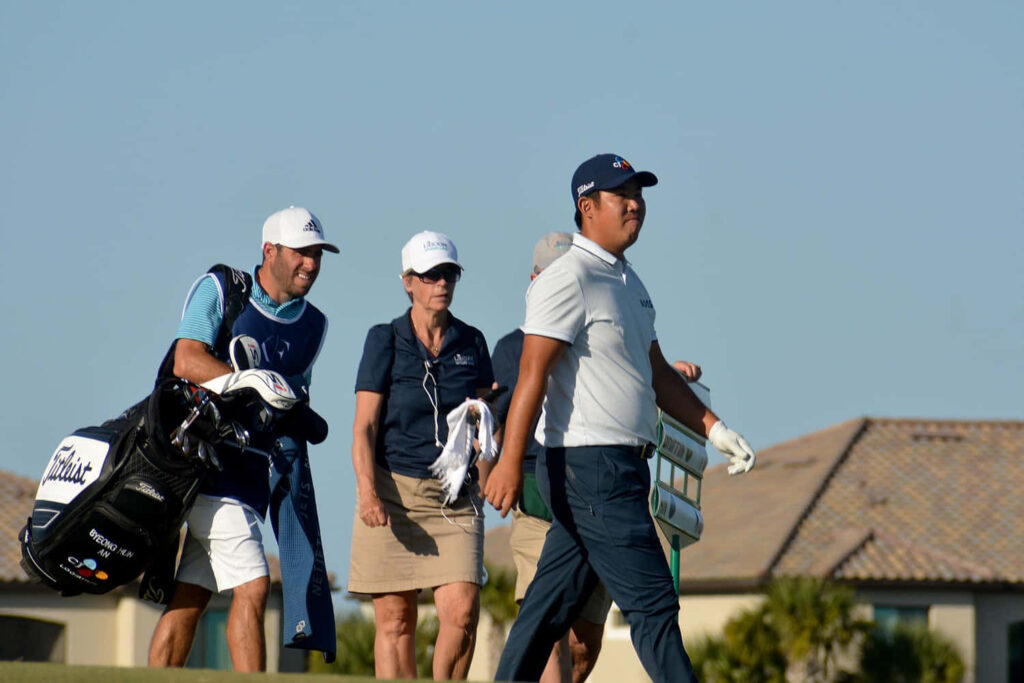 An Byeong-hun and caddie walking on sunny golf course with blue skies suburban homes background Wallpaper