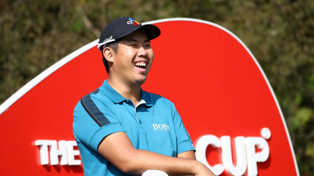 An Byeong-hun smiling at The CJ Cup in blue polo and cap with vibrant red CJ Cup sign background Wallpaper