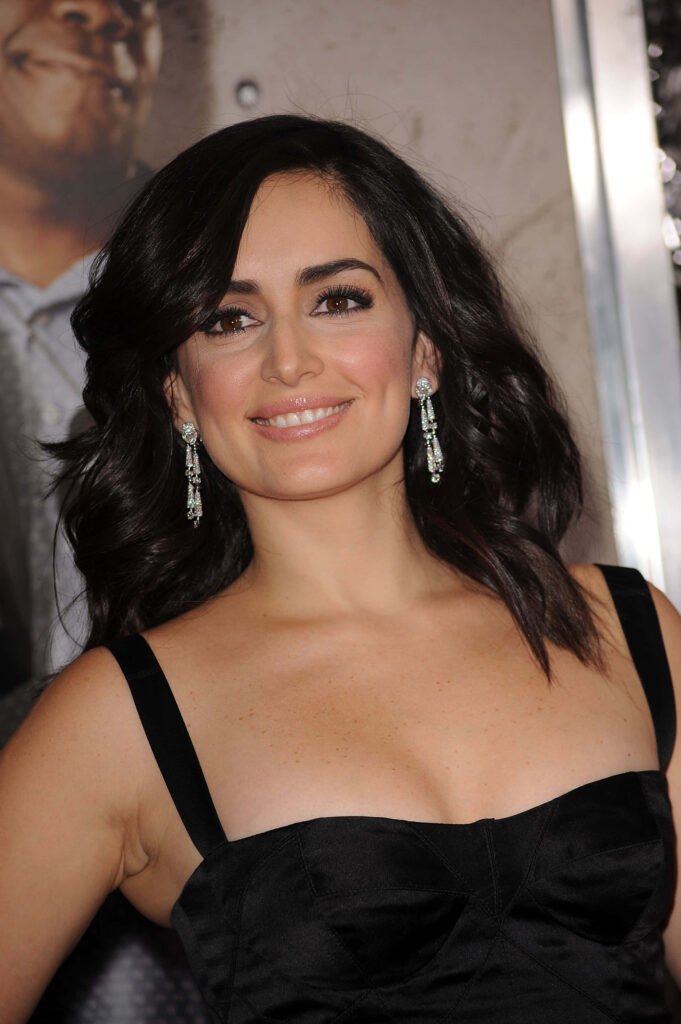 Ana de la Reguera smiling confidently in black dress posing at event with wallpaper backdrop