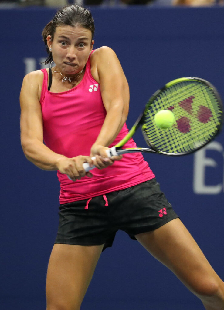 Anastasija Sevastova focused hitting tennis ball during intense match with wallpaper background