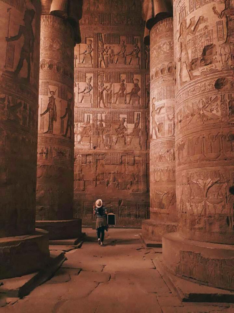 Tourist exploring ancient Egyptian temple interior with towering hieroglyphic columns and sunlight Wallpaper