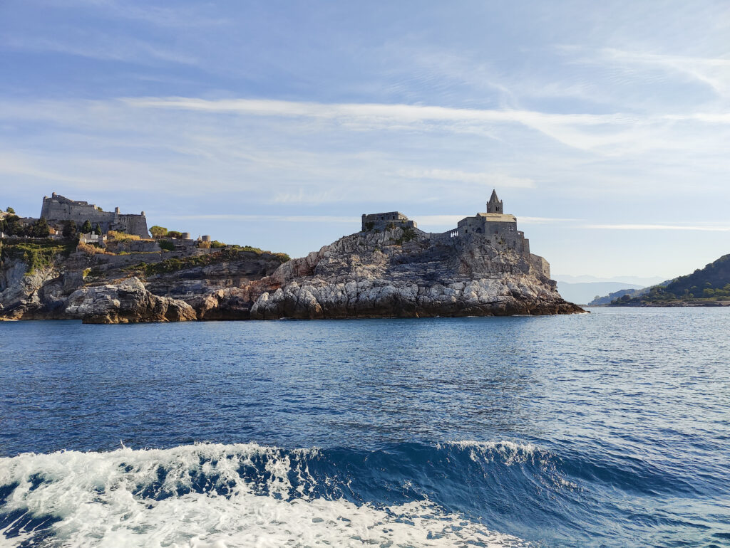Ancient stone tower on rocky island surrounded by blue sea green cliffs and clear sky wallpaper