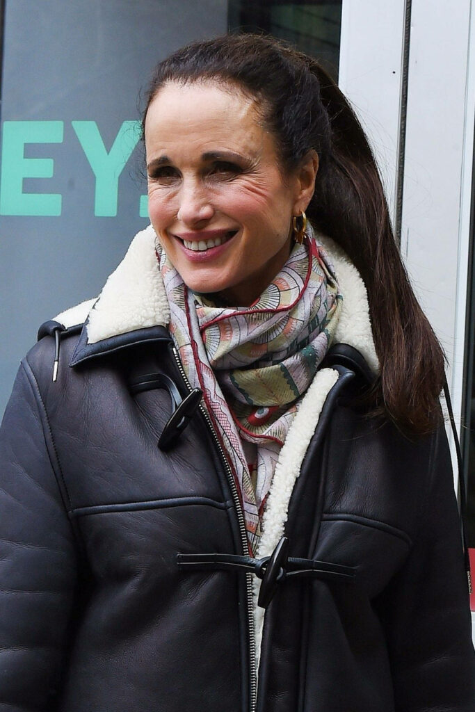 Andie MacDowell smiling in cozy shearling jacket and patterned scarf with wallpaper background