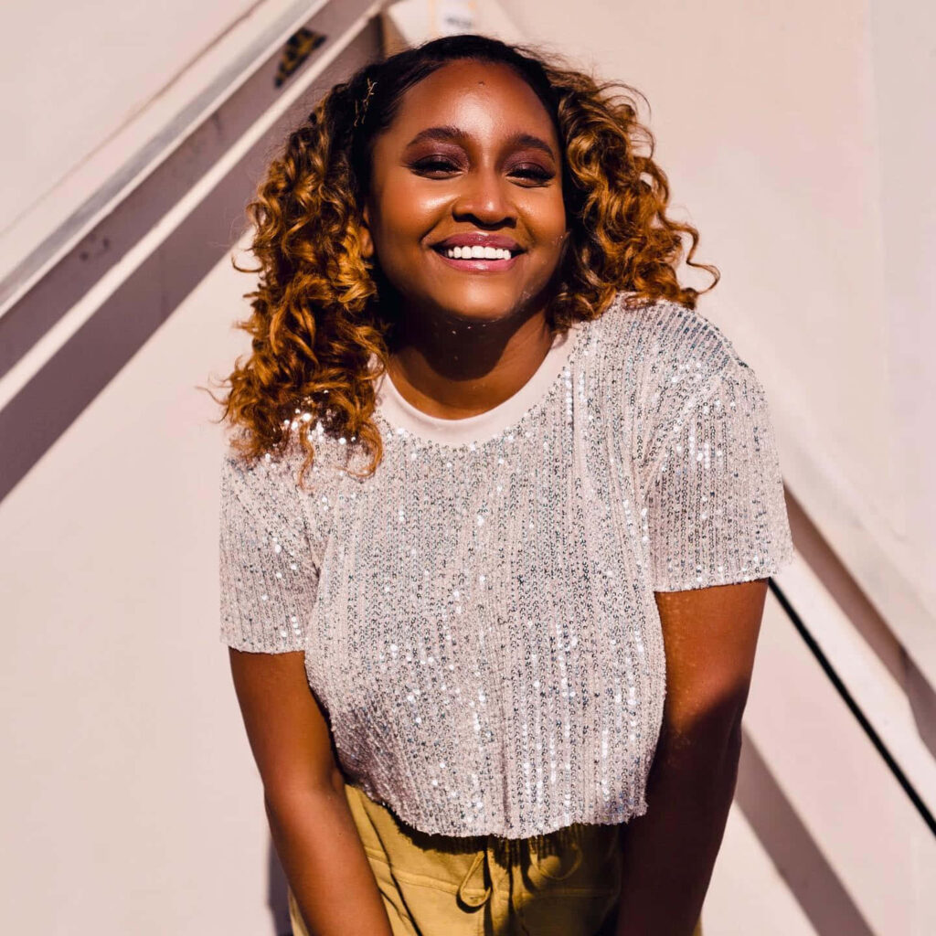 Andrea Lewis smiling brightly in sparkling silver sequin top against a wallpaper background