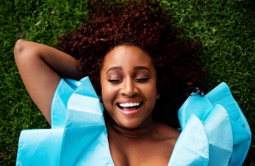 Andrea Lewis smiling happily lying on green grass resting head on blue pillow outdoors nature Wallpaper