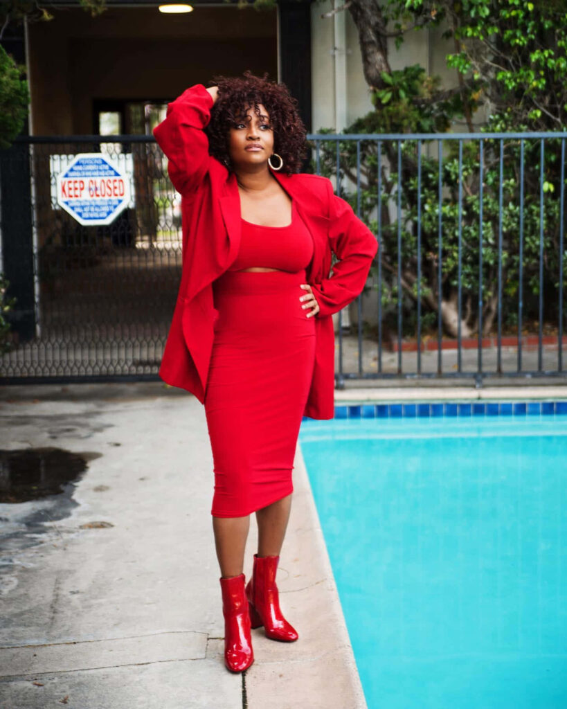 Andrea Lewis in bold red outfit with skirt top jacket and glossy boots by vibrant poolside Wallpaper