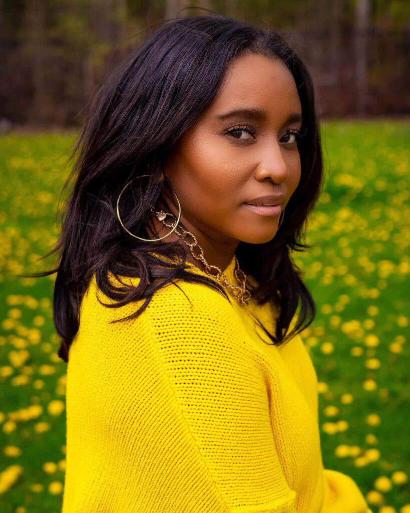 Andrea Lewis in vibrant yellow sweater standing in sunny field of yellow flowers cheerful scene Wallpaper