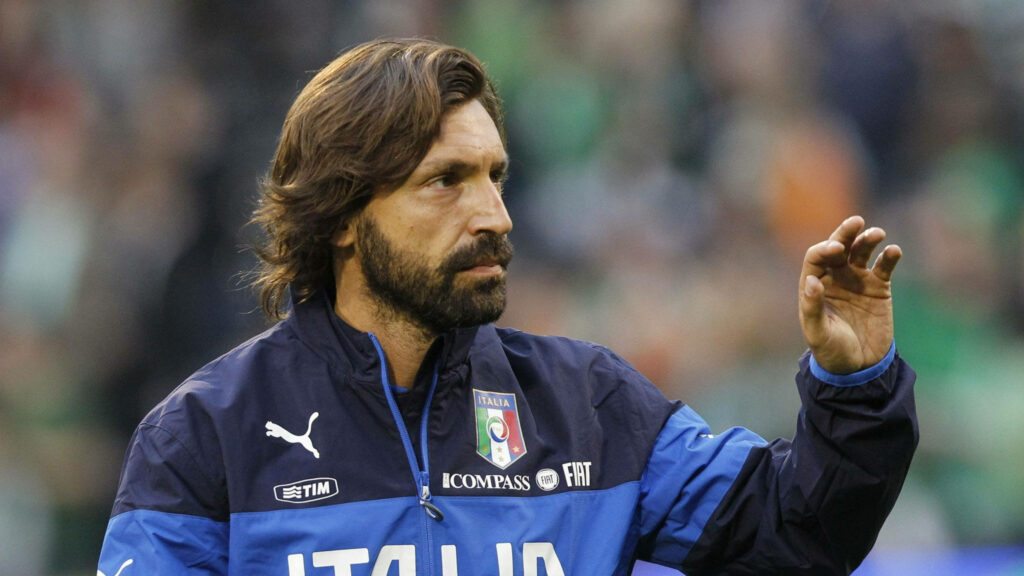 Andrea Pirlo in Italy training jacket making hand gesture on field blurred stadium background Wallpaper