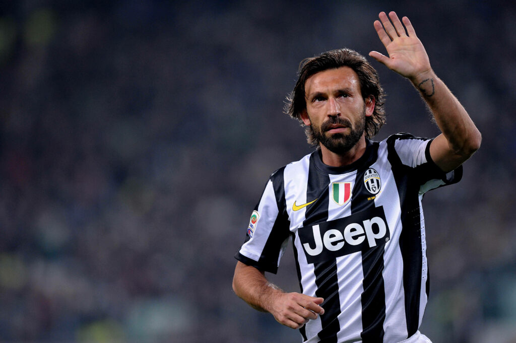Andrea Pirlo in Juventus jersey raising hand on field with blurred stadium crowd background wallpaper