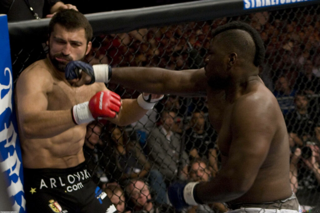 Andrei Arlovski receiving a powerful punch during intense MMA fight inside octagon ring action Wallpaper