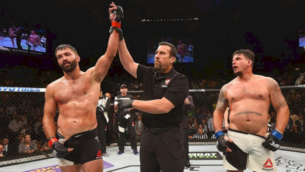 Andrei Arlovski wins five round rematch with arm raised by referee in the octagon fight background Wallpaper