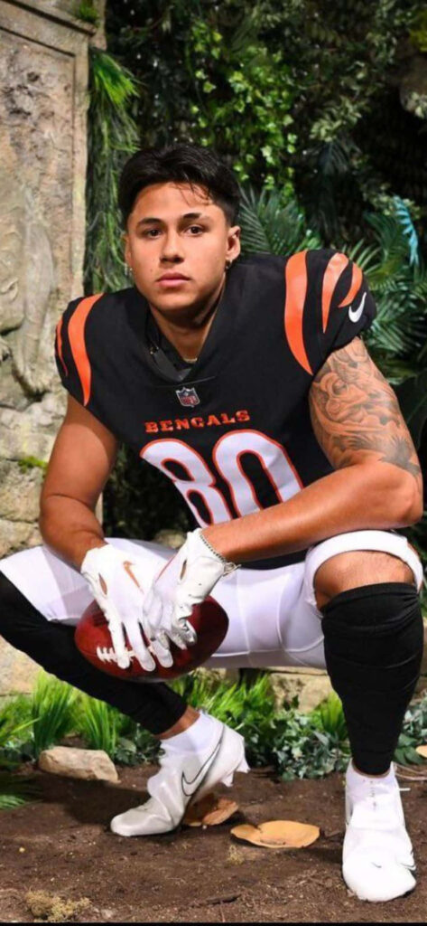 Andrei Iosivas in Bengals uniform kneeling with football against jungle wallpaper background