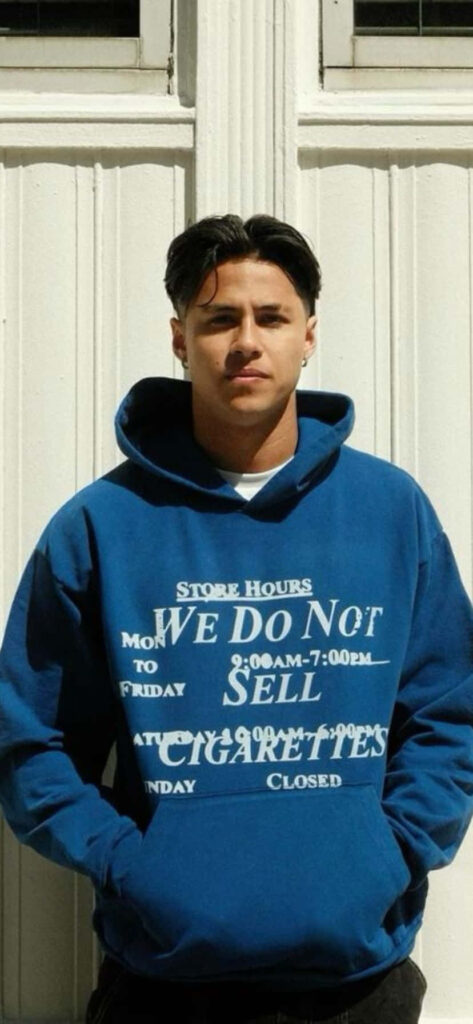 Andrei Iosivas in blue hoodie with bold text posing stylishly against a white door background Wallpaper