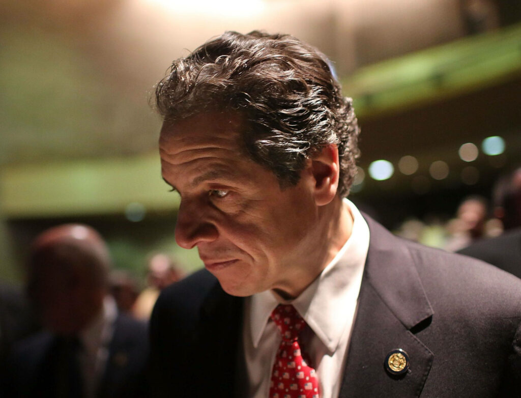 Andrew Cuomo thoughtful side profile in suit and red tie against soft professional background wallpaper