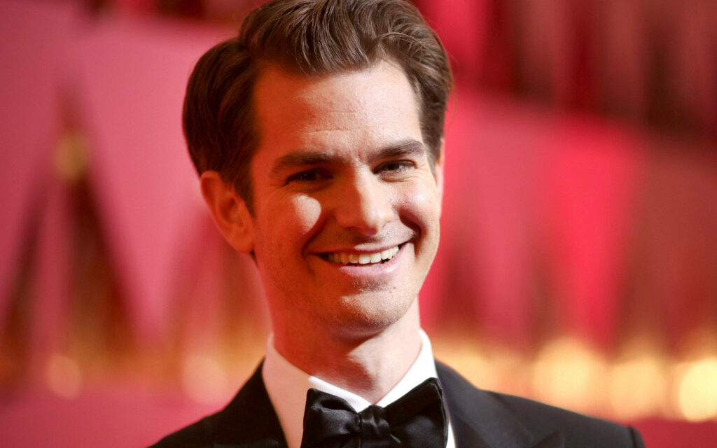 Close-up of Andrew Garfield smiling in a suit with soft red background wallpaper background
