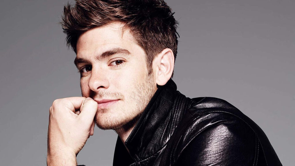 Andrew Garfield confident in leather jacket posing with hand on chin against grey background Wallpaper