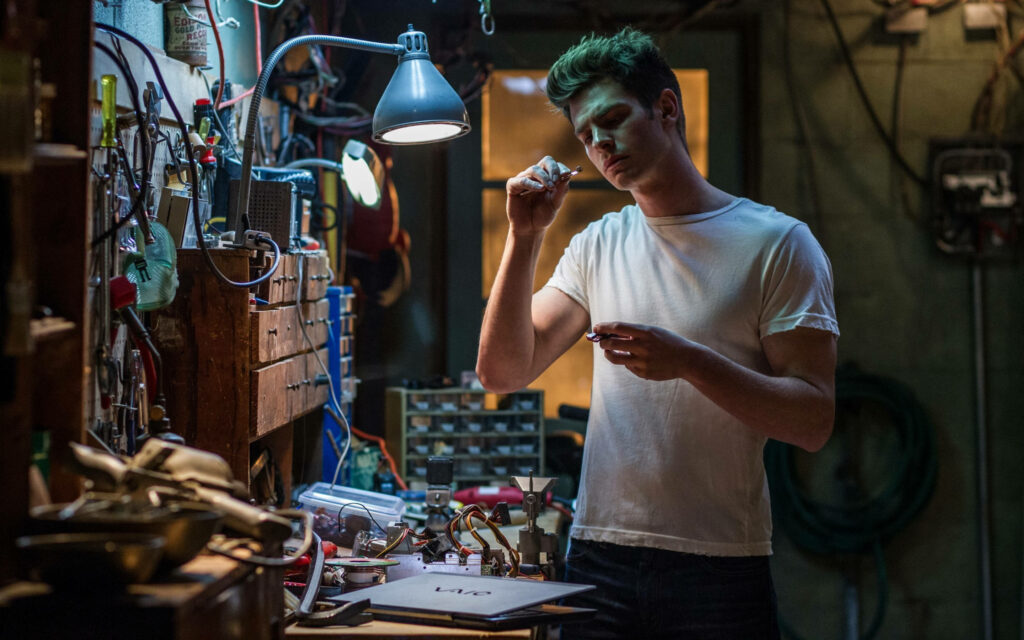 Andrew Garfield as Peter Parker focused on tech gadget at cluttered workbench detailed wallpaper