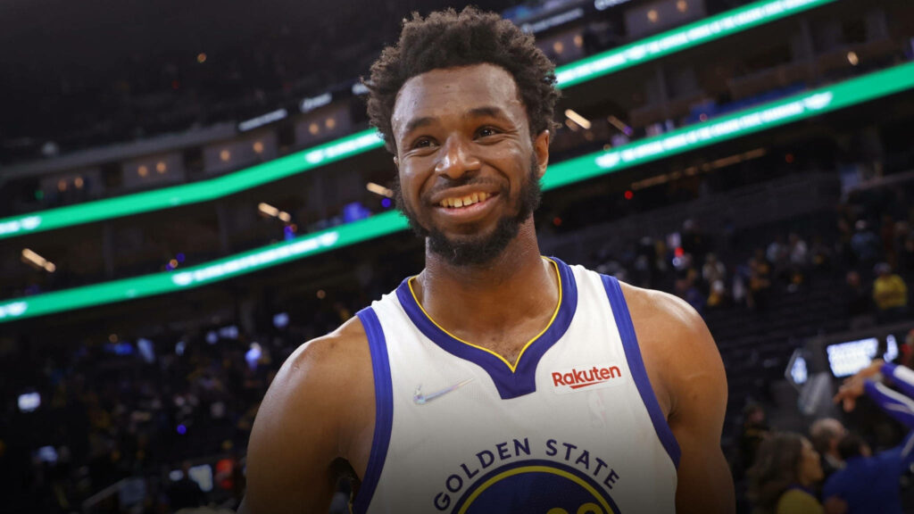 Andrew Wiggins smiling in Golden State Warriors jersey on basketball court lively arena background Wallpaper