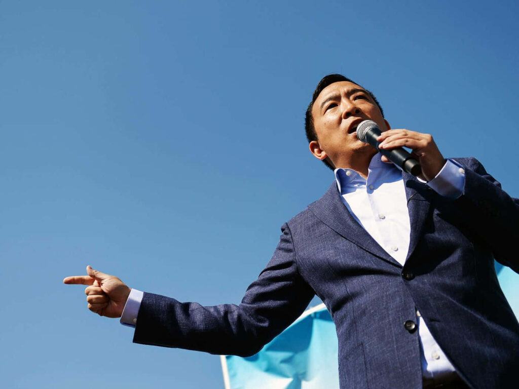 Andrew Yang speaking confidently into microphone outdoors promoting Universal Basic Income advocacy Wallpaper
