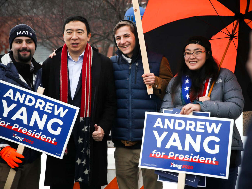 Andrew Yang smiling with supporters holding Andrew Yang for President campaign signs outdoors Wallpaper