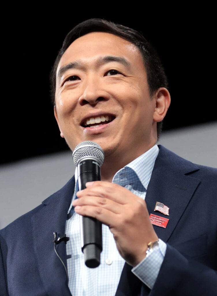 Andrew Yang confidently speaking on stage holding microphone engaging audience wallpaper background