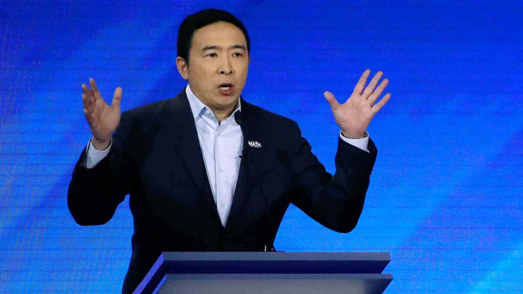 Andrew Yang speaking passionately at debate podium with hands raised against blue background Wallpaper