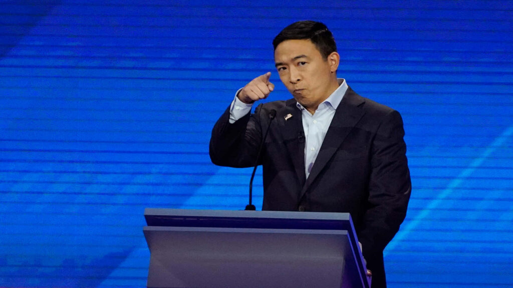 Andrew Yang focused and assertive speaking behind debate podium on blue background intense emotion Wallpaper