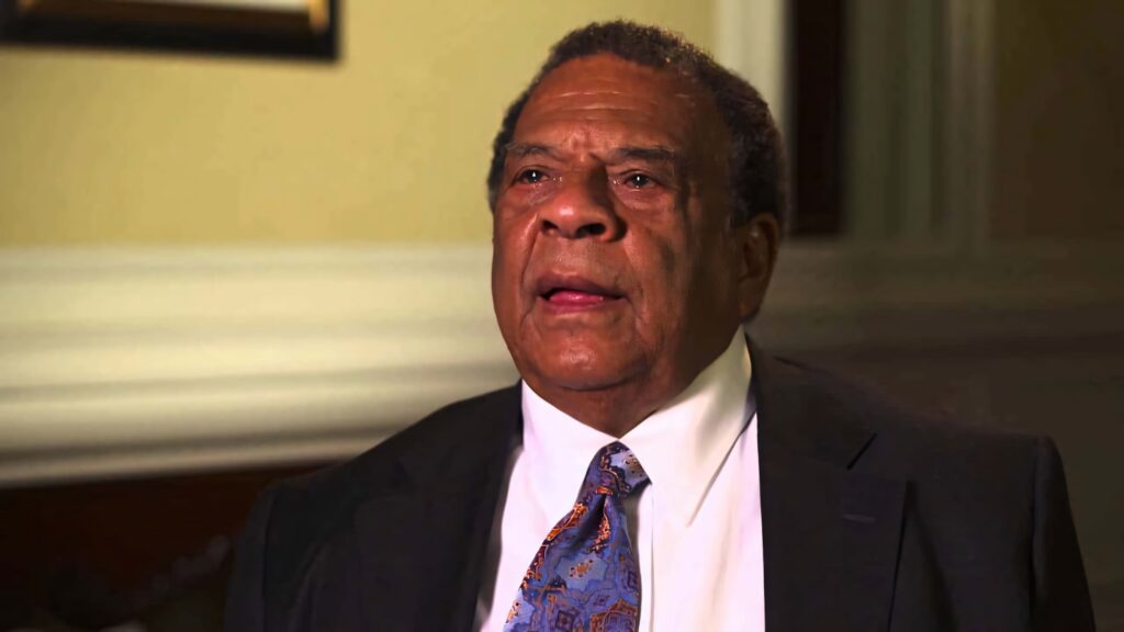 Andrew Young speaking in interview warmly lit room neutral wallpaper background seated