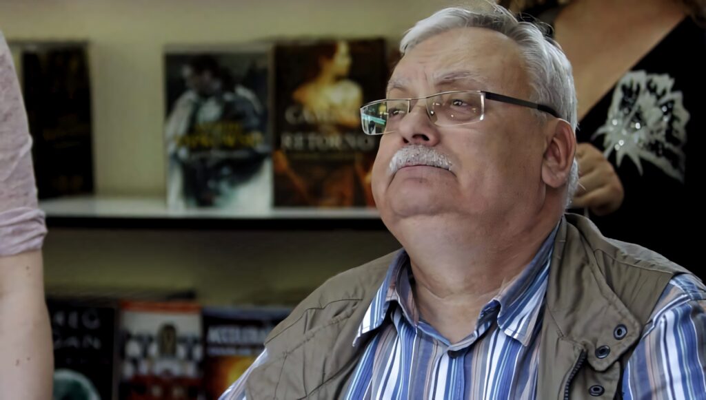Andrzej Sapkowski signing books at event surrounded by novels inspiring fans wallpaper background