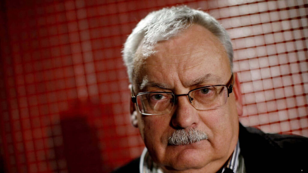 Portrait of Andrzej Sapkowski with serious expression and red grid background wallpaper