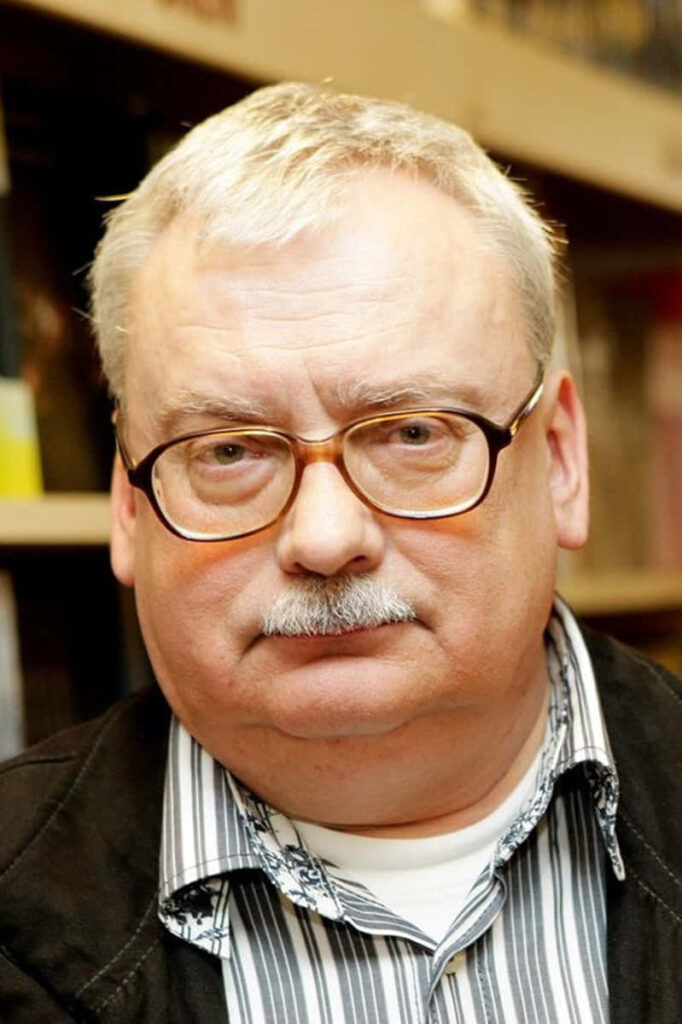 Portrait of Andrzej Sapkowski author with serious expression and bookshelf background wallpaper