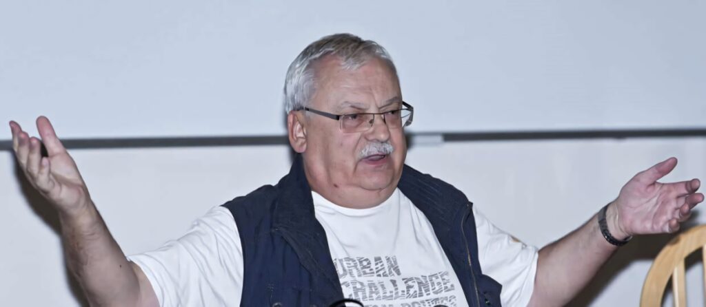 Andrzej Sapkowski speaking passionately with expressive gestures in a scholarly setting wallpaper