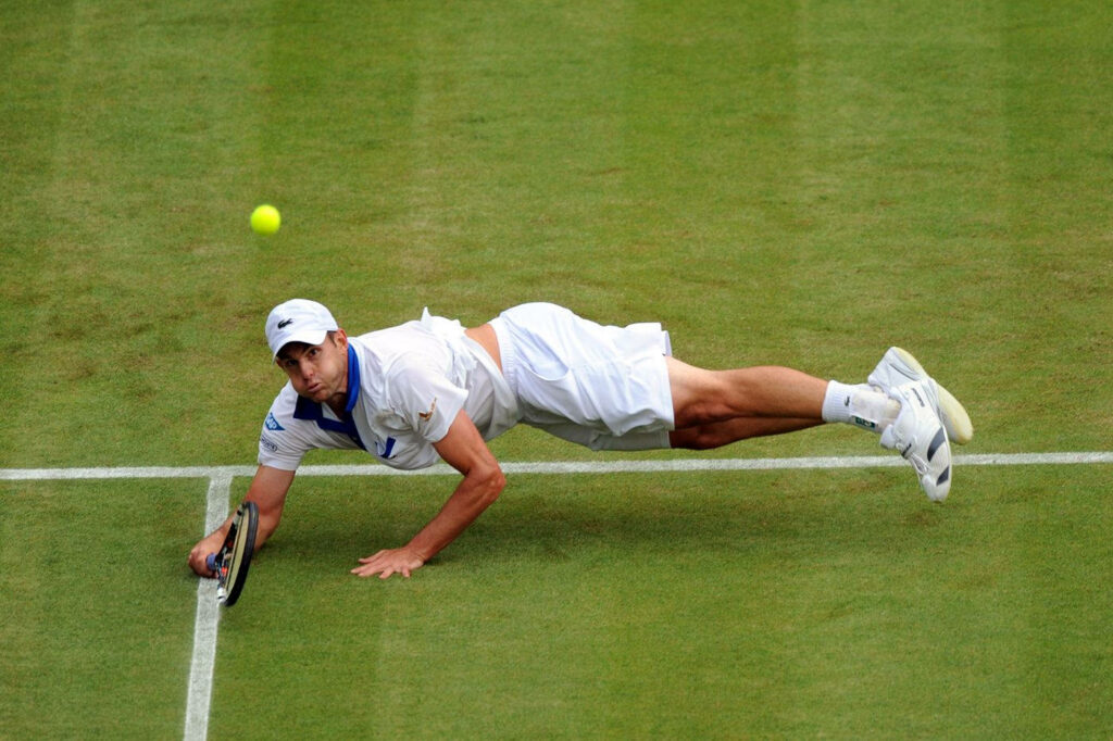 Andy Roddick diving to return a tennis shot on grass court during intense high stakes match wallpaper