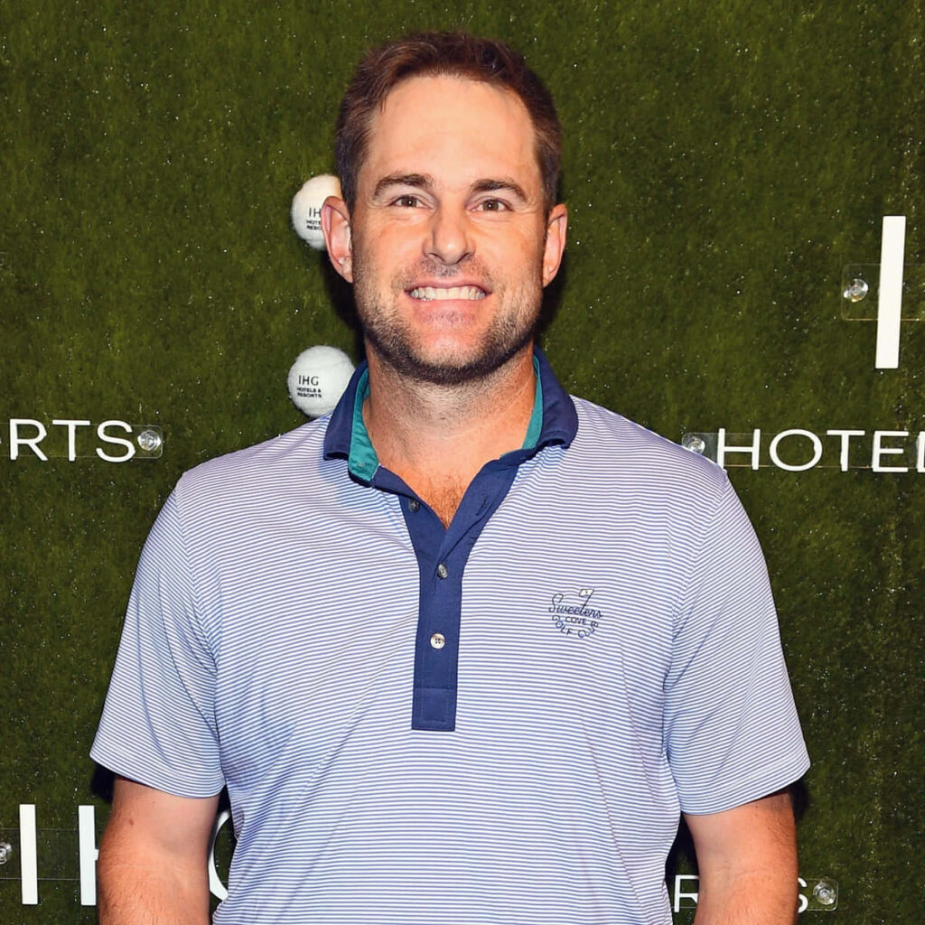 Andy Roddick smiling in striped polo shirt against green textured wallpaper background