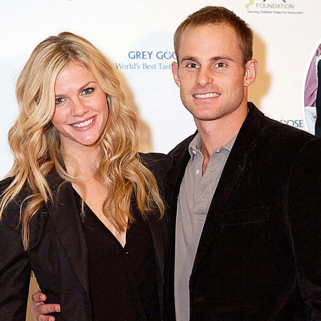 Andy Roddick and wife smiling stylishly posing together at public event with wallpaper background