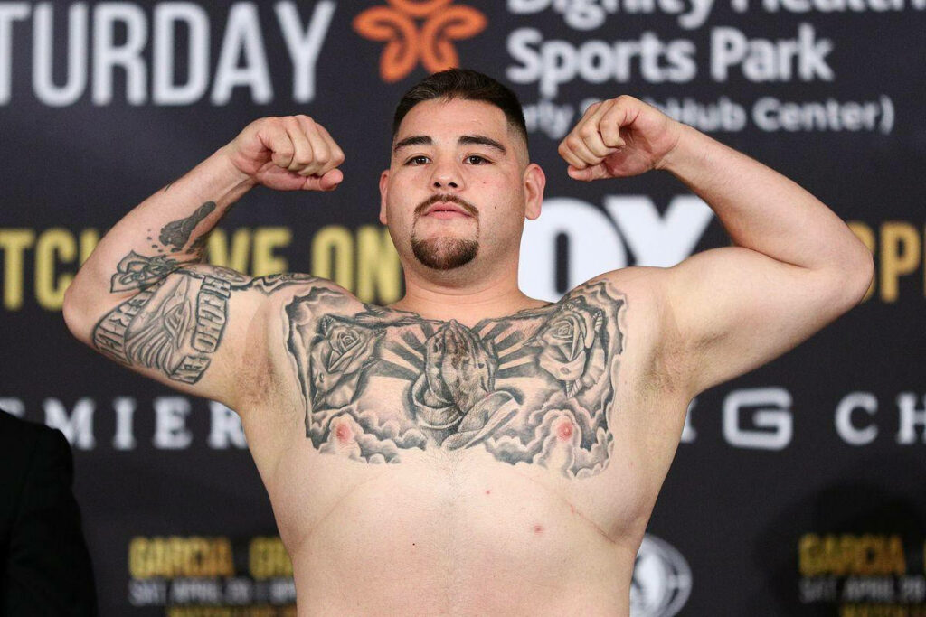 Andy Ruiz Jr confident weigh-in pose showing tattoos determination with event promo banners background Wallpaper